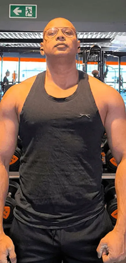 Ashish staat voor een rek met dumbbells, met zijn gezicht naar de camera