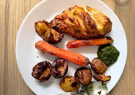 Een bord met gebraden kip, zoete aardappel, wortel en een groene saus